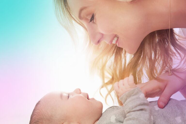 White woman leaning over a baby and smiling at the baby.
