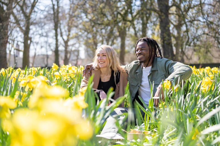 Smiling young couple sitting in field of yellow daffodils