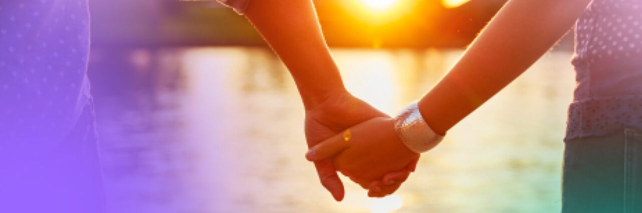 Two people holding hands with sunset