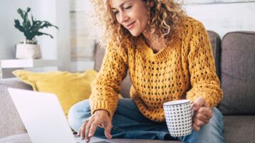 Blonde woman sitting down using her laptop with a mug 