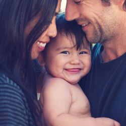 Interracial couple  smiling whilst both holding smiling baby in the middle