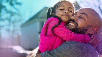 Black single man hugging young daughter, smiling  