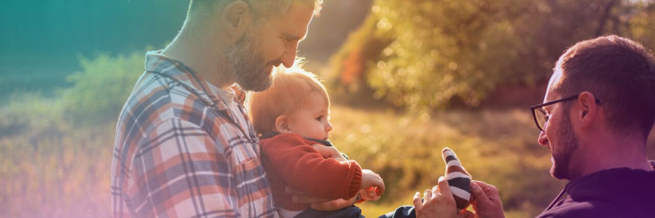 White, same sex male couple holding baby and putting on sock.