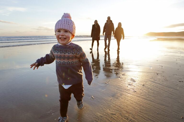 Family on a beach, little girl running ahead with pink hat on smiling