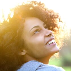 Woman with dark curly hair looking up to the sky smiling