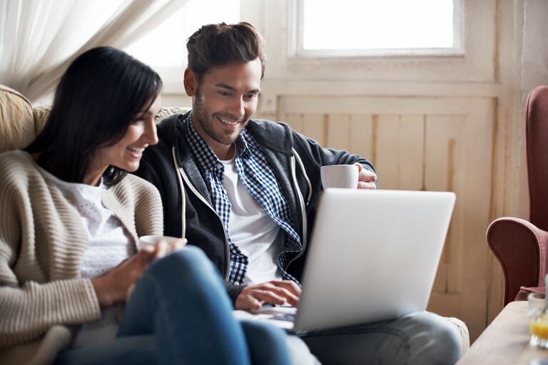 Couple smiling together using a laptop and drinking tea