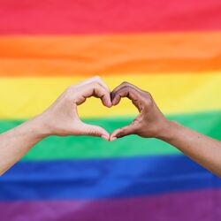 two hands meeting in a heart shape in front of the pride flag