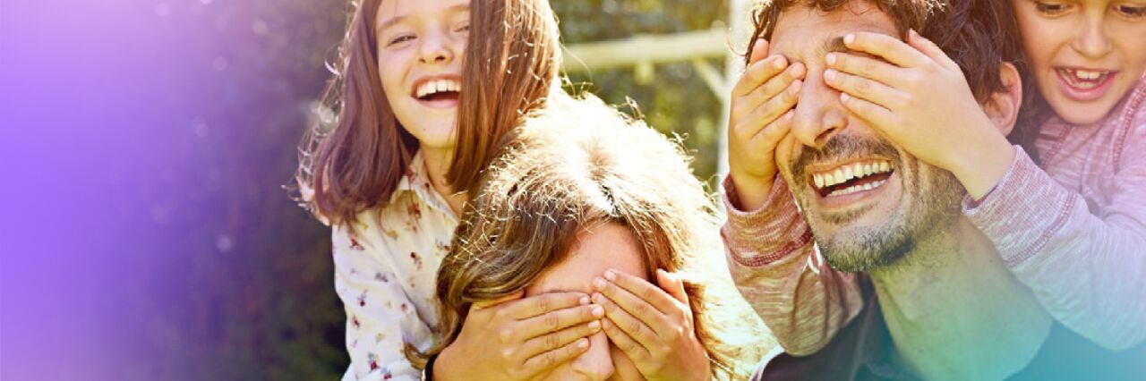 White heterosexual couple each carry boy and girl child on their back and the children are covering their eyes.