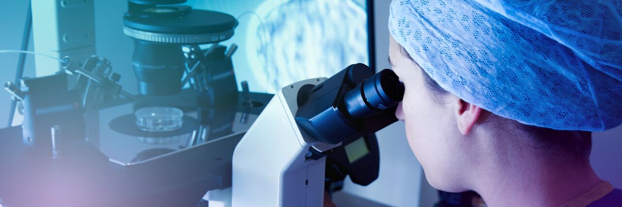 Over shoulder view of embryologist looking down microscope at an embryo