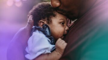 Black  father holding baby to chest and kissing forehead